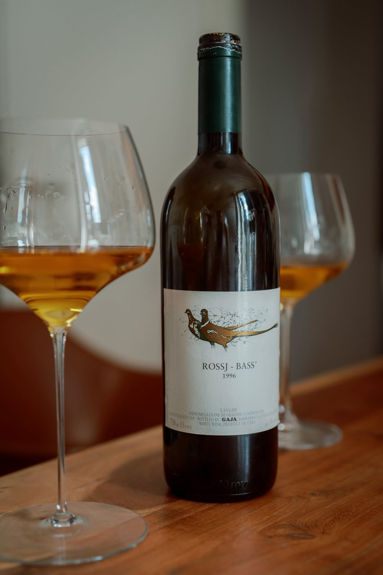 Gaja Rossj-Bass 1996 Langhe in two Manufaktur Vitis Chardonnay glasses, the wine deep amber-gold, on a wooden table