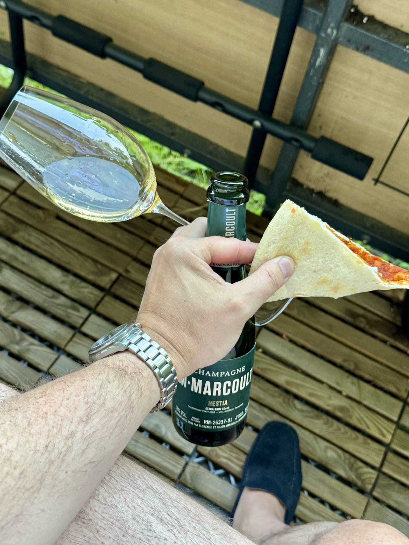 Champagne Marcoult Hestia Extra Brut split next to a Riedel Champagne glass, paired with a slice of pizza on the terrace