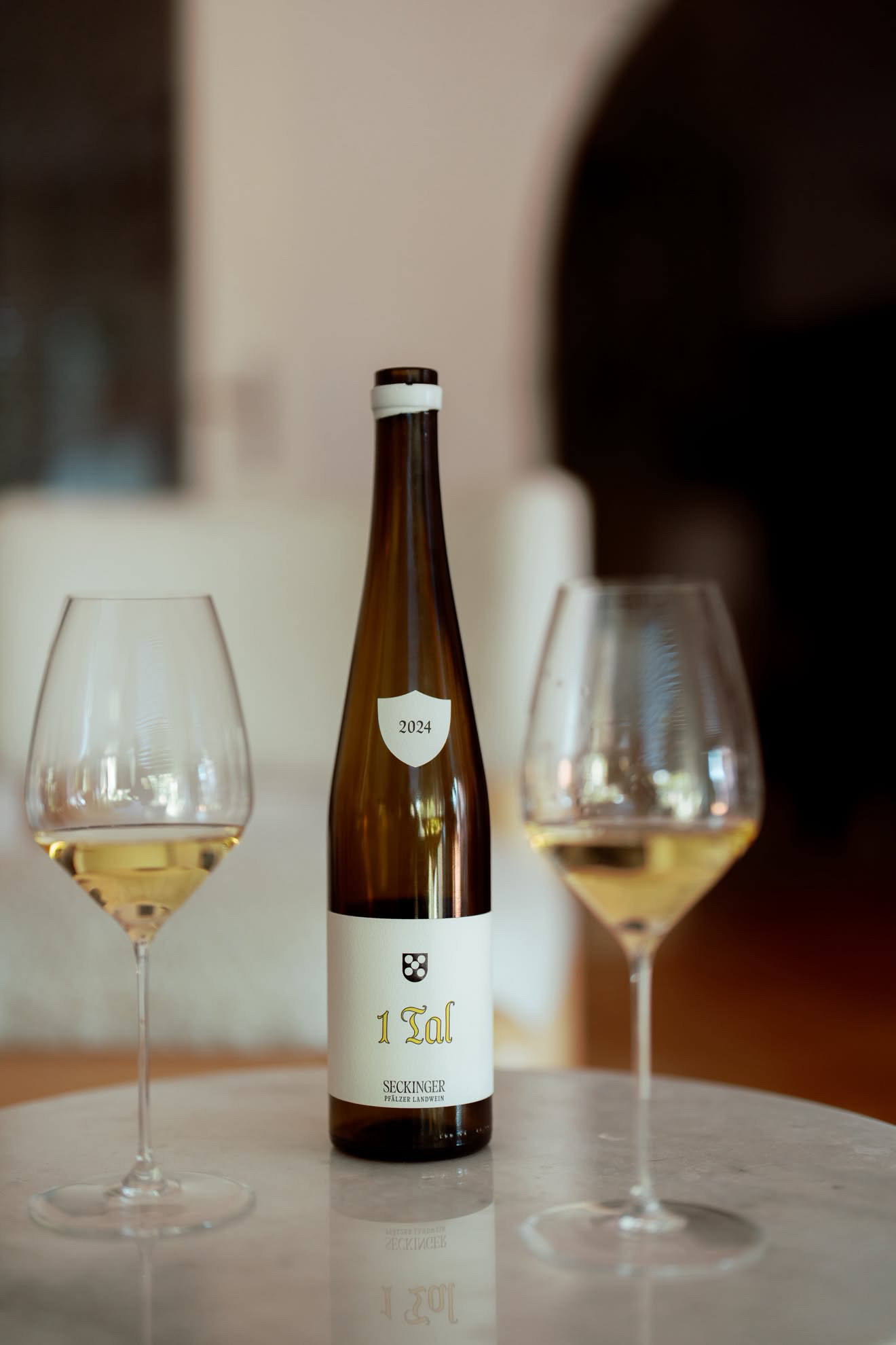 Seckinger 1 Tal 2024 Pf&auml;lzer Landwein between two Riedel Veloce Riesling glasses on a marble table in soft daylight