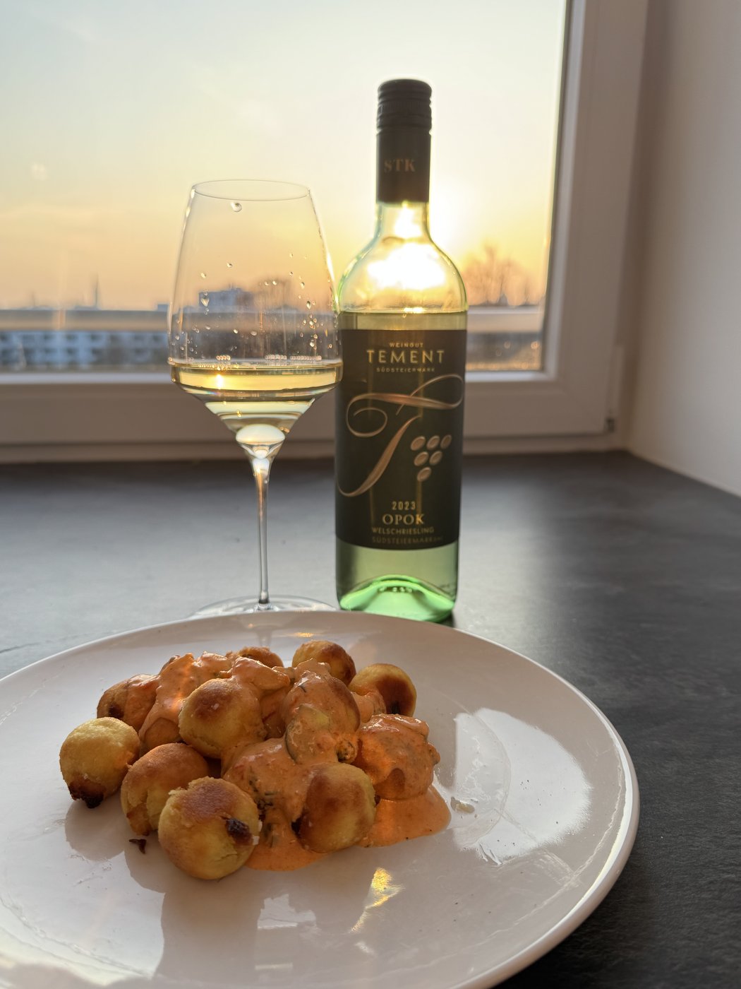 Tement Ried Opok Welschriesling 2023 at golden hour in a Manufaktur Vitis Riesling glass, paired with savoury Krapfen by the window