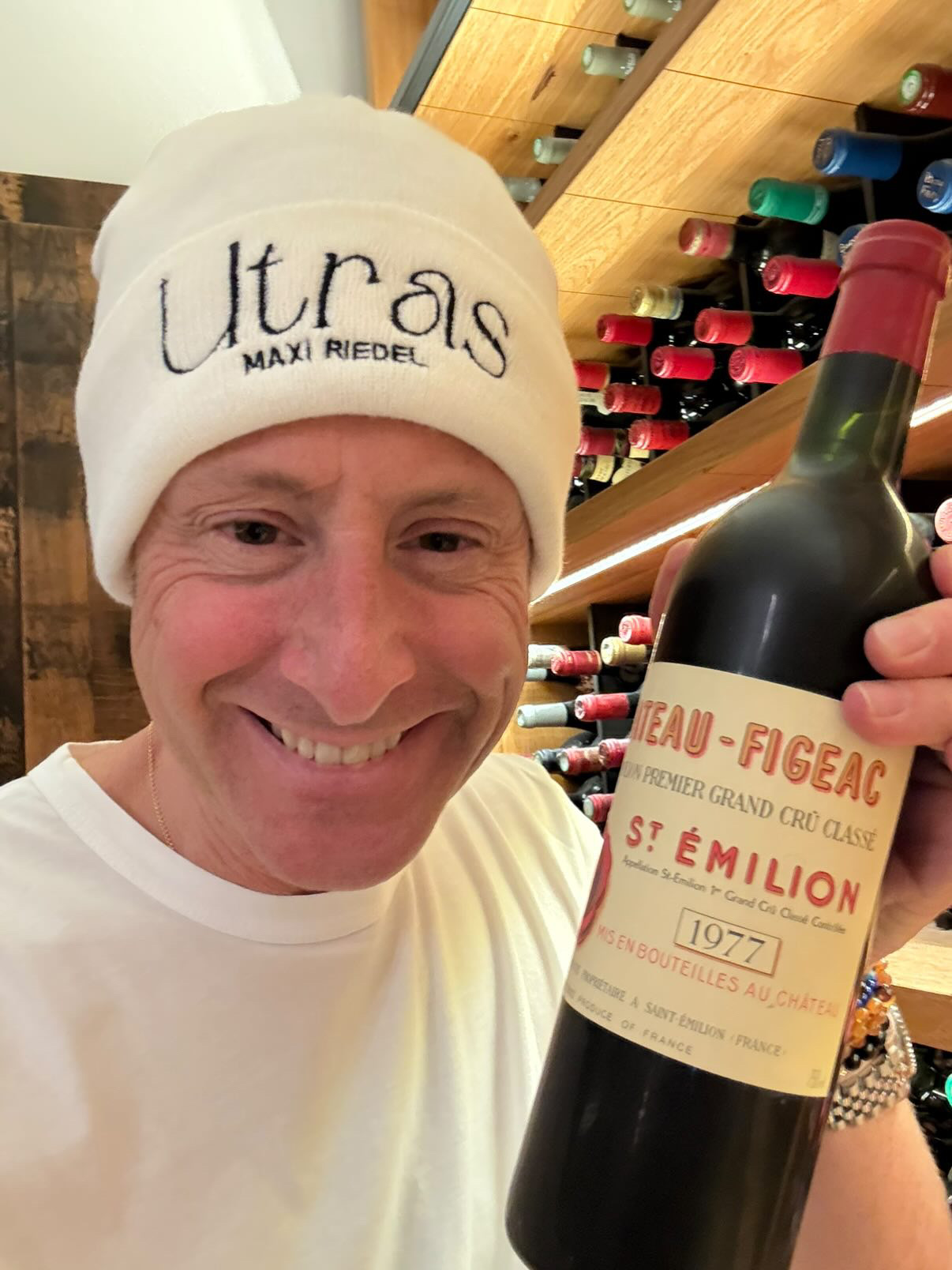 Maximilian Riedel wearing the Ultras Maxi Riedel beanie in a wine cellar, holding a Château Figeac 1977 Saint-Émilion